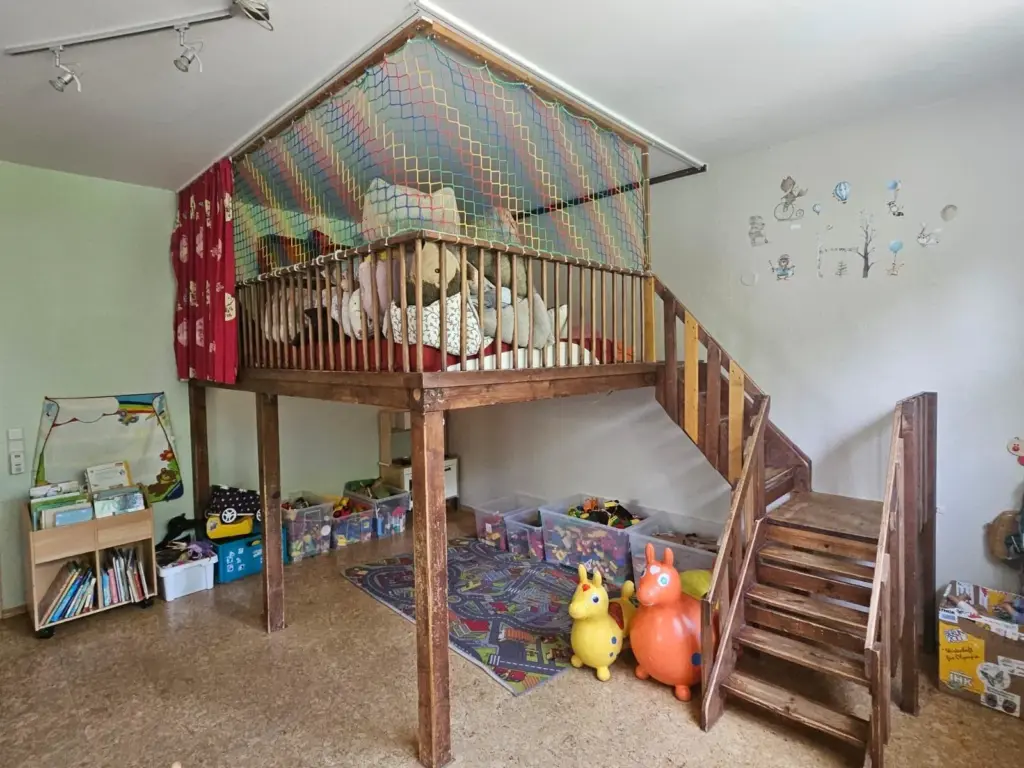 Die Hochebene mit vielen Kissen. Da drunter ist ein Autoteppich, zwei Spielpferde und andere Spielsachen