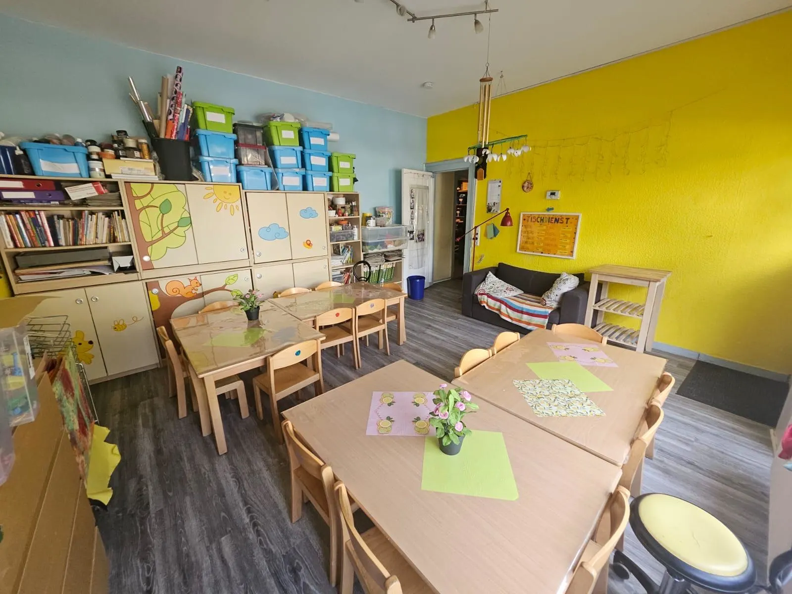 Tische mit Stühlen. Im Hintergrund eine offene Tür bei einer gelben Wand