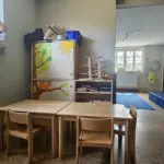 Zwei kleine Tische mit ein paar Stühlen. Im Hintergrund der Durchgang zu einem anderen Zimmer mit blauer Matte